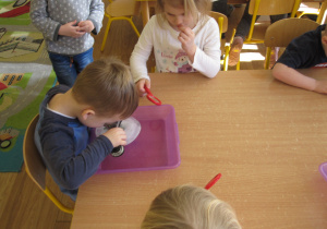 Dzieci oglądają przez lupę dinozaury w lodzie