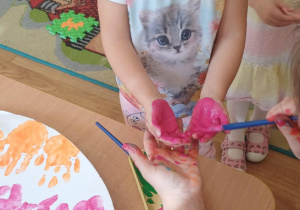 Dziewczynka z grupy pierwszej ma malowane ręcę, które odciśnie na wielkanocnej pisance