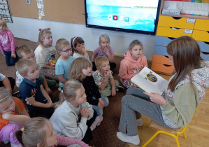 Dzieci słuchają książki czytanej przez absolwentkę przedszkola
