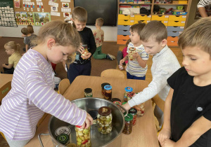Dzieci wkładają słoiki do garnka
