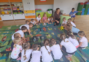 Dzieci z grupy III turlają piłkę a jeden chłopiec biegnie wokół nich