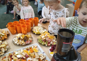 Dzieci z grupy II wkładają owoce do sokowirówki