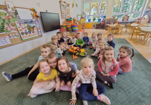 Dzieci z grupy II siedzą na dywanie wokół owoców