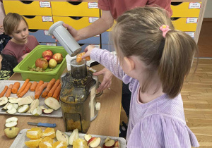 Dziewczynka z grupy IV dodaje owoce do sokowirówki