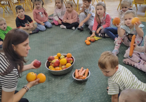 Dzieci z grupy II siedzą na dywanie wokół owoców