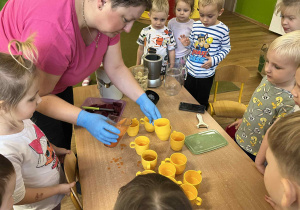 Dzieci z grupy I czekają, aż pani Ania naleje sok do kubeczków