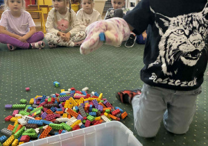 Dzieci próbują przenosić klocki rękawiczkami kuchennymi