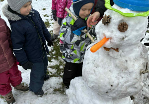 Dzieci patrzą jak chłopiec wbija patyk w bałwana