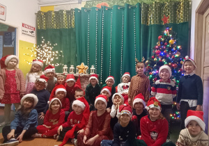 Dzieci z grupy IV stoją przed ścianką świąteczną