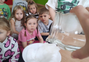 Dzieci obserwuja jak nauczycielka filtruje ropzuszczony śnieg