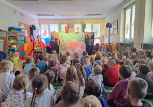 Dzieci siedzą na dywanie podczas oglądania spektaklu