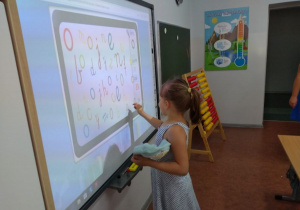 dziewczynka robi zadanie na tablicy multimedialnej w szkole podstawowej