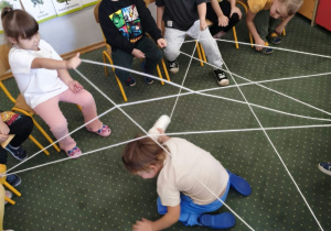 Dzieci przechodzą pod pajęczą siecią z włóczki