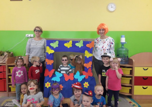 Dzieci z grupy I wraz z nauczycielkami siedzą przy swojej fotobudce ozdobionej motylkami
