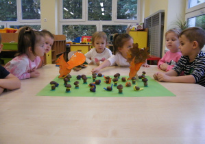 Dzieci siedzą wokół projektu makiety, na której są już gotowe grzyby, ślimaki i wiewiórki