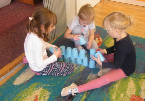 Trzy dziewczynki układają budowlę z niebieskich kubków