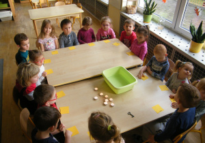 Dzieci z grupy II siedzą wokół stołu i czekają na lanie wosku