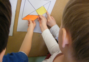 Dzieci z grupy III sprawdzają gdzie powinni przykleić mniejsze figury geometryczne, aby powstał duży kwadrat