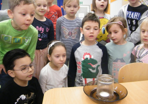 Dzieci obserwują świeczkę, która zakryta jest szklanką