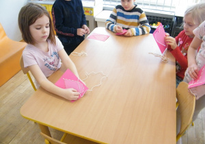 Dzieci z grupy V przeplatają sznurek przez swoje walentynkowe serca
