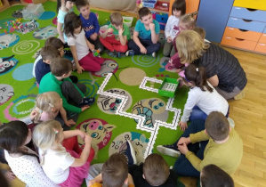 Przedszkolaki z grupy IV razem z panią obserwują drogę ozobota wyznaczoną przez ułożone puzzle przez dzieci