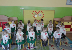 Przedszkolaki z grupy I siedzą na krzesełkach, ubrane w białe koszule