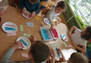 Piątka dzieci wykonuje zadanie matematyczne - za pomocą patyczków w dwóch kolorach ilustruje działanie zapisane przez nauczyciela