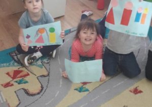 Troje dzieci prezentuje swoje prace - rodzina z figur geometrycznych