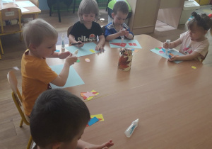 Czwórka dzieci nakleja na kartkę figury geometryczne