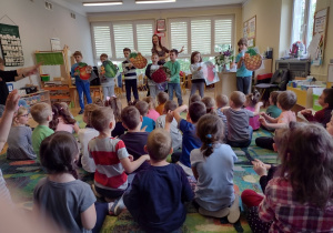 Siedmioro dzieci tańczy w rytm piosenki z planszami, na których są owoce