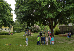 W oddali widać przedzkolaki, które biorą udział w róznych konkurencjach sportowych w ogrodzie przedszkolnym