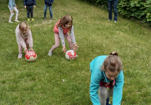 Trzy dziewczynki z grupy V toczą piłkę pod górkę