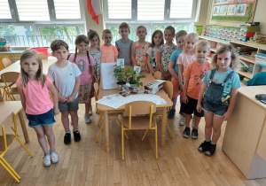Dzieci z grupy V stoją przt stoliku na którym rozłożopne są nagrody za konkurs plastyczny o wiośnie