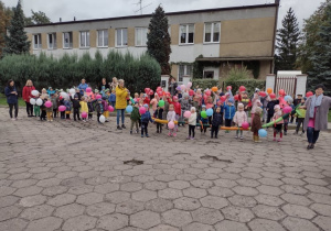 Wszystkie dzieci z przedszkola stoją przed budynkiem przedszkola i ustawiają się w pary przed przemarszem z okazji Dnia Przedszkolaka