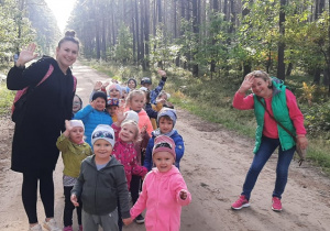 Przedszkolaki z grupy III wraz z wychowawczyniami machają do aparatu stojąc na leśnej ścieżce