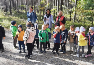Dzieci z grupy II wraz z nauczycielkami stoją na leśnej ścieżce i piją wodę z kubeczków