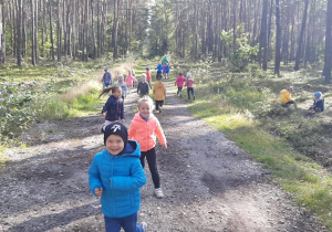 Dzieci z grupy III biegają po lesnej ścieżce szukając leśnych skarbów