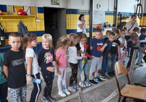 Dzieci stoją w rzędzie i przekazują sobie wąż gaśniczy