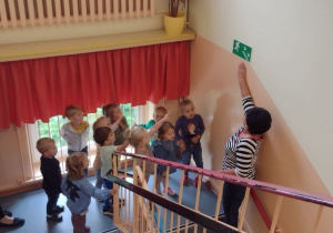 Pani z I grupy pokazuje dzieciom znak ewakuacyjny na schodach