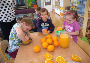 Dwóch chłopców i jedna dziewczynka wyciskają sok z pomarańczy