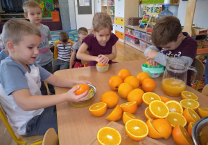 Dwóc chłopców i jedna dziewczynka wyciskają sok z pomarańczy