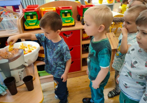Dzieci przyglądają się jak chłopiec wkłada pomarańczę do sokowirówki