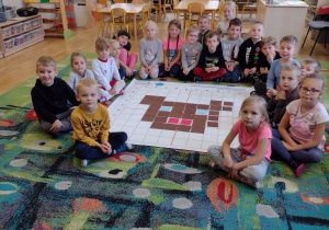 Dzieci z grupy V siedzą wokół obrazka powstałego na macie do kodowania z kwadratów - głowy misia