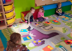 Czworo dzieci siedzi na dywanie ze swoimi pracami