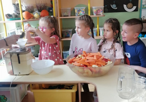 Dzieci patrzą jak dziewczynka wkłada marchewkę do sokownika