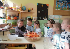 Dzieci przyglądają się jaki owoc wybierze dziewczynka, aby wrzucić go do sokownika