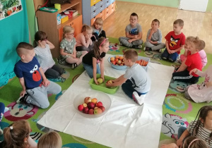 Dzieci siedzą w kole i przyglądają sie jak dwoje z nich myje jabłka