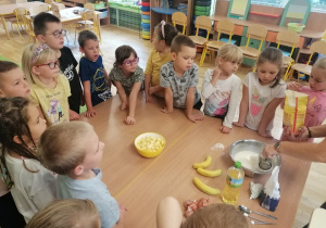 Dzieci przyglądają się jak pani dosypuje mąkę do ciasta