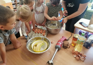 Dzieci przyglądają się jak dziewczynka dodaje do ciasta jajko