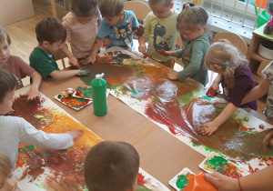Dzieci mieszają rękami różne kolory farb po dużeym kartonie